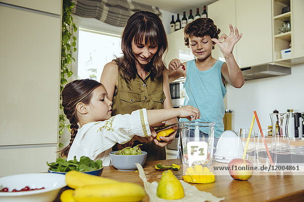 Mutter und Kinder legen Früchte in einen Smoothie-Mixer