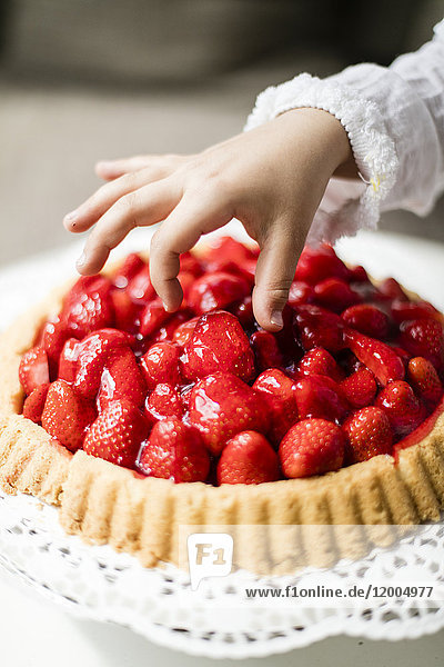 Girl's hand taking strawberry from cake