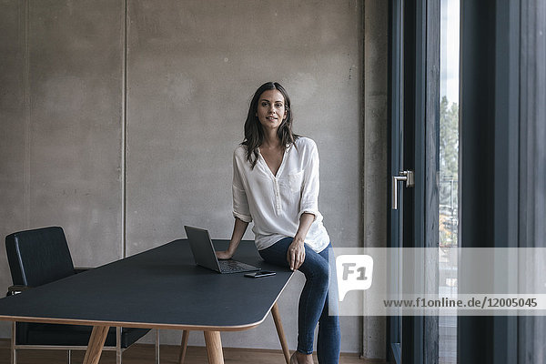 Portrait of smiling woman sitting on table with laptop and cell phone