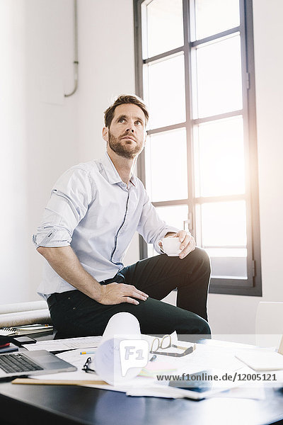 Portrait of architect with cup of coffee sitting on desk in his office