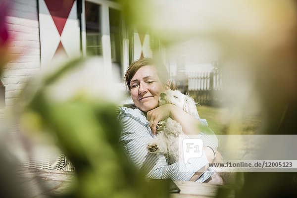 Frau kuschelt mit Hund auf der Terrasse