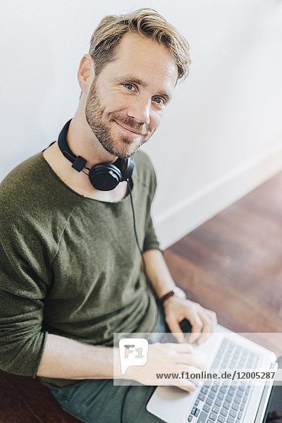 Porträt eines lächelnden Mannes mit Kopfhörer und Laptop