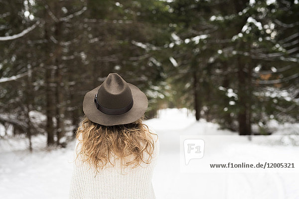 Rückansicht der jungen Frau mit Hut und Strickpullover im Winterwald
