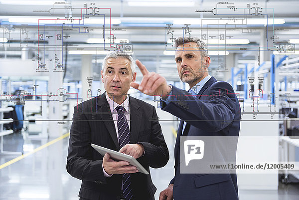 Two businessmen looking at graphic on glass pane in factory hall