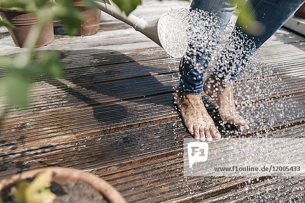 Frau mit Gießkanne  die Wasser über ihre Füße gießt.