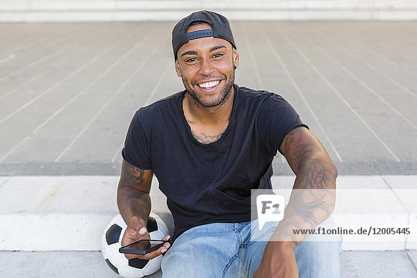 Porträt eines lachenden jungen Mannes mit Smartphone