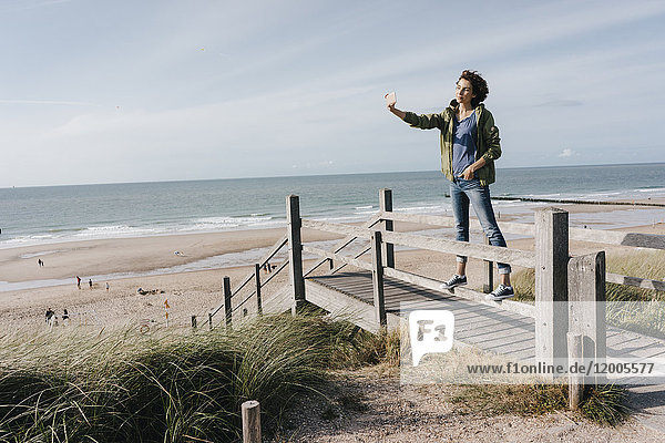 Frau  die auf einer Strandpromenade am Strand steht und einen Selfie nimmt.