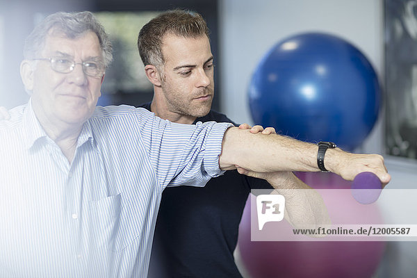 Senior man exercising with dumbbell at physio's practice