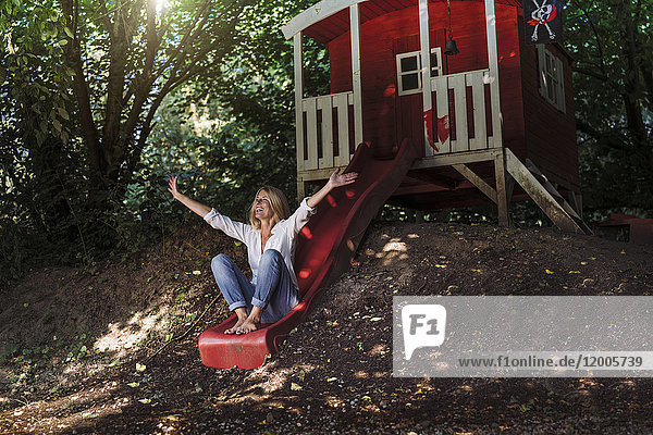 Mature woman sitting on slide in front of garden shed in the woods