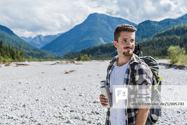 Germany  Bavaria  portrait of young hiker with backpack holding thermos flask
