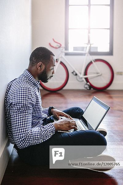 Man using laptop sitting on wooden floor with bicycle in background