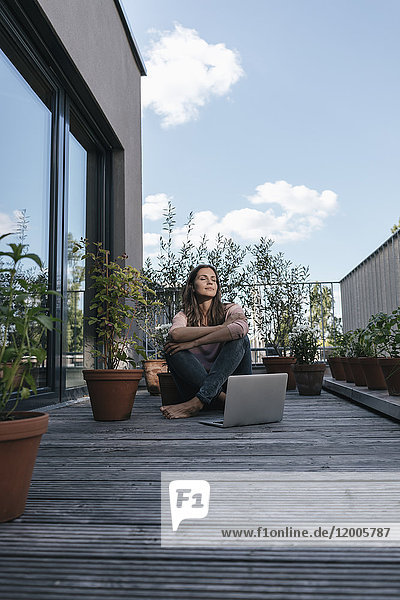 Frau mit Laptop auf dem Balkon sitzend