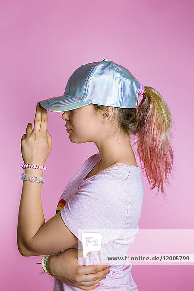 Stilvolle junge Frau mit gefärbtem Haar,  die eine Basecap vor rosa Hintergrund trägt.