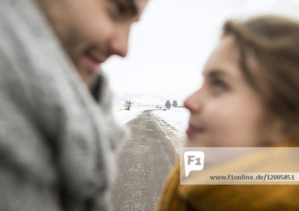 Leere Landstraße in verschneiter Landschaft mit jungem verliebten Paar im Vordergrund