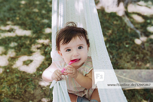 Portrait of hungry baby girl with spoon in mouth in the garden