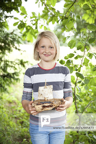 Porträt eines lächelnden Mädchens mit geschnitztem Holzboot im Wald