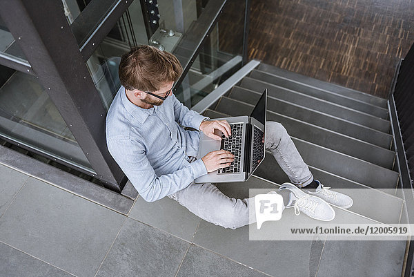 Mann mit Laptop auf der Treppe im Büro sitzend