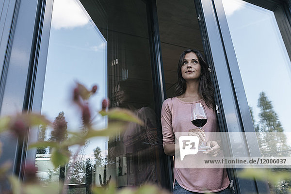 Frau hält ein Glas Rotwein und schaut aus dem Fenster.