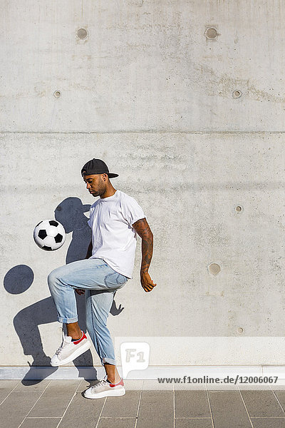Young man playing with soccer ball in front of concrete wall