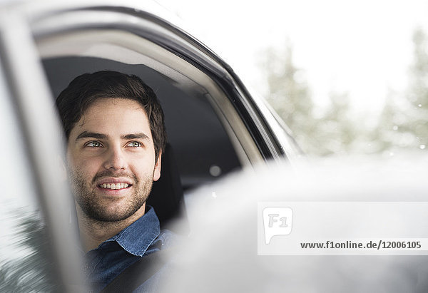Porträt eines lächelnden jungen Mannes beim Autofahren im Winter