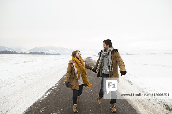 Verliebtes junges Paar geht auf leerer Landstraße in verschneiter Landschaft spazieren