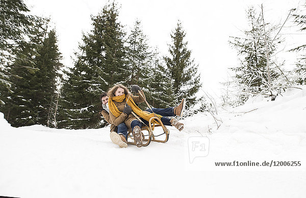 Happy young couple on sledge in winter forest