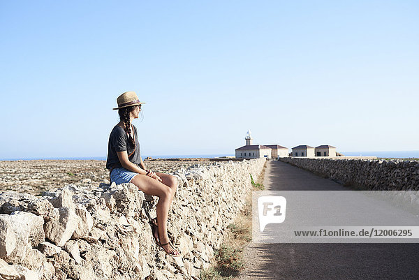 Spanien  Menorca  Einzelreisender auf Natursteinmauer sitzend mit Blick auf die Aussicht