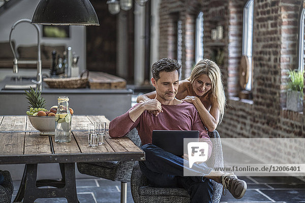 Glückliches Paar in der Landhausküche mit Blick auf den Laptop