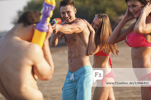 Glückliche Freunde beim Spielen mit Wasserpistolen am Strand