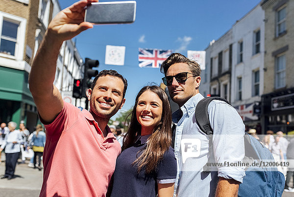 UK  London  Portobello Road  Porträt von drei Freunden  die Selfie mit dem Smartphone nehmen.