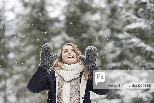 Porträt der glücklichen jungen Frau bei Schneefall in der Natur