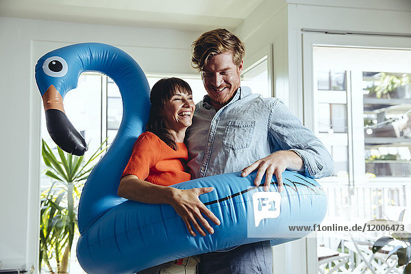 Happy couple holding an inflatable flamingo at home