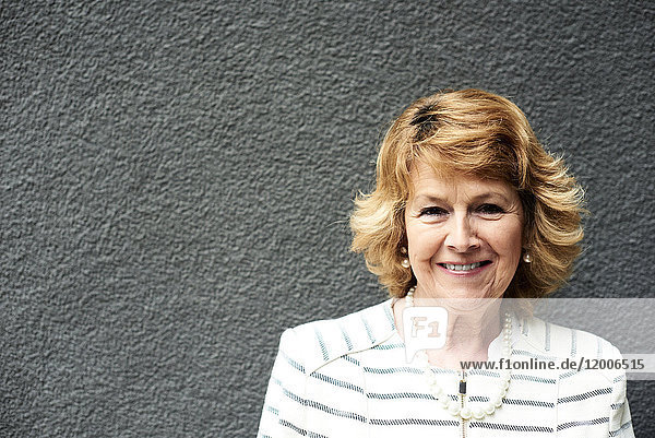 Portrait of smiling senior businesswoman against grey wall