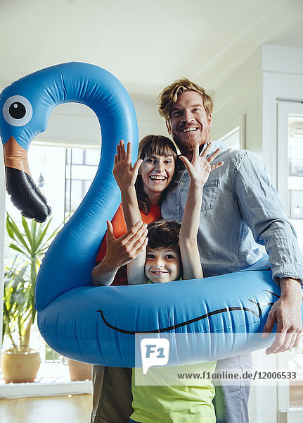 Glückliche Eltern mit einem Sohn  der zu Hause einen aufblasbaren Flamingo hält.