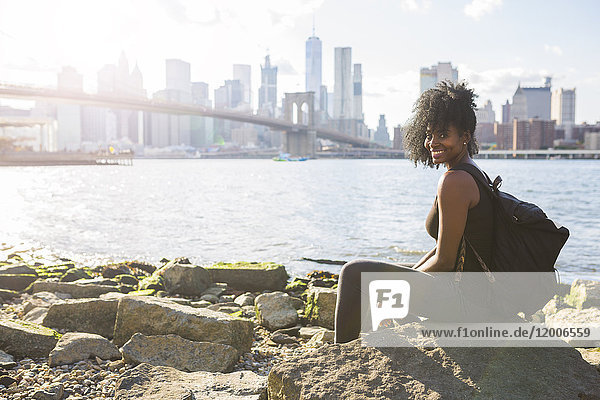 USA  New York City  Brooklyn  Porträt einer lächelnden Frau am Wasser sitzend
