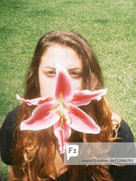 Junge erwachsene Frau mit Orchideenblüte im Mund