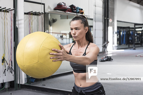 Mixed race woman lifting heavy ball in gymnasium