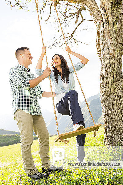 Mann hilft Frau auf Baumschaukel