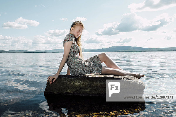 Kaukasisches Teenager-Mädchen sitzt auf einem Felsen im Meer