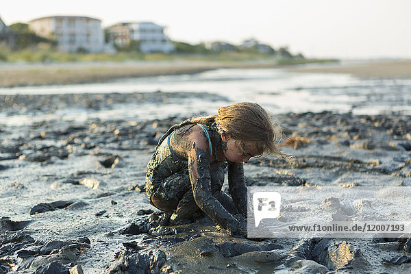 Kaukasisches Mädchen mit Schlamm bedeckt  das am Strand spielt