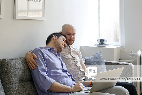 Kaukasische Männer  die sich auf dem Sofa umarmen und einen Laptop benutzen