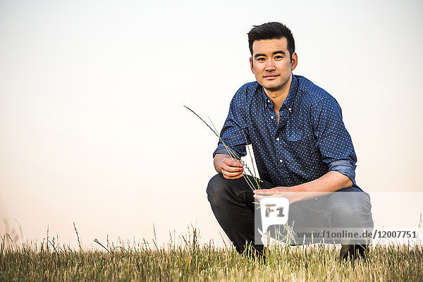 Chinesischer Mann hockt im Feld und hält Gras