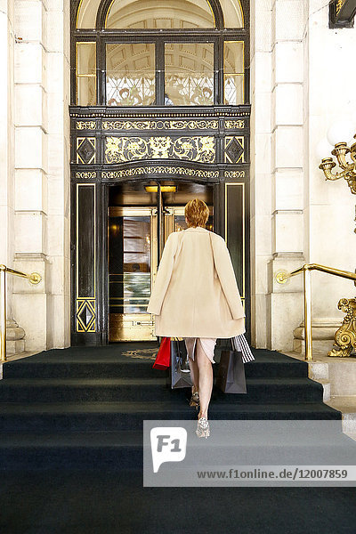 Glamouröse kaukasische Frau trägt Einkaufstaschen zum Luxusgebäude