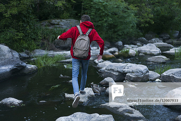 Kaukasischer Mann geht auf Felsen und überquert einen Fluss