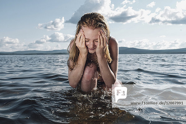 Kaukasisches Teenager-Mädchen kniet im Meer und spritzt sich Wasser ins Gesicht