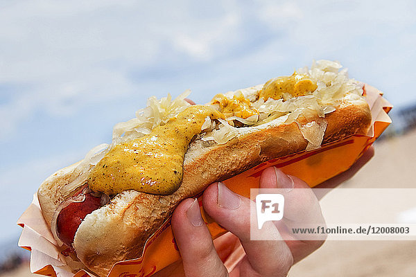Hand holding hot dog with mustard and sauerkraut