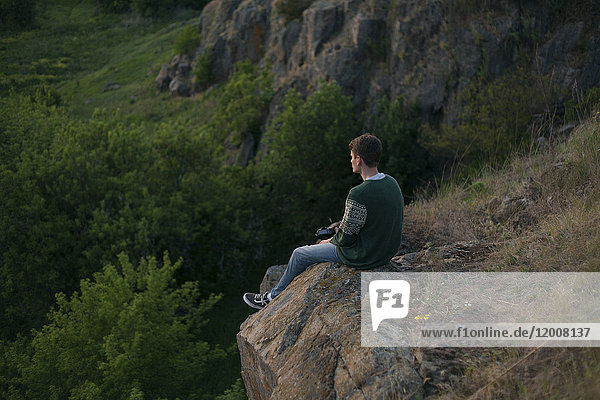 Kaukasischer Mann sitzt auf einem Felsen und bewundert die Landschaft