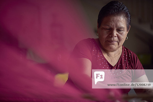 Hispanic woman weaving fabric on loom