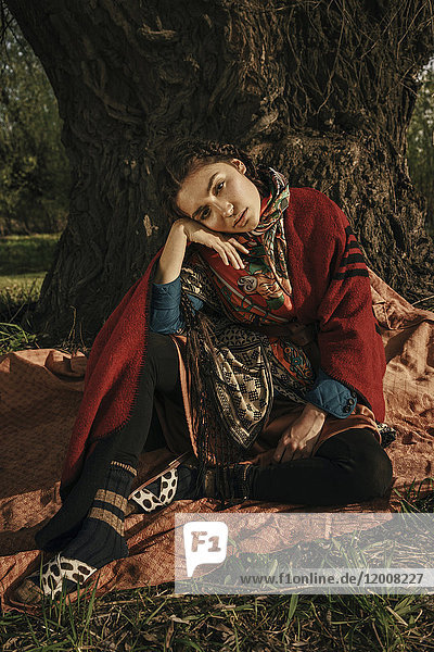 Kaukasische Frau in traditioneller Kleidung sitzt in der Nähe eines Baumes