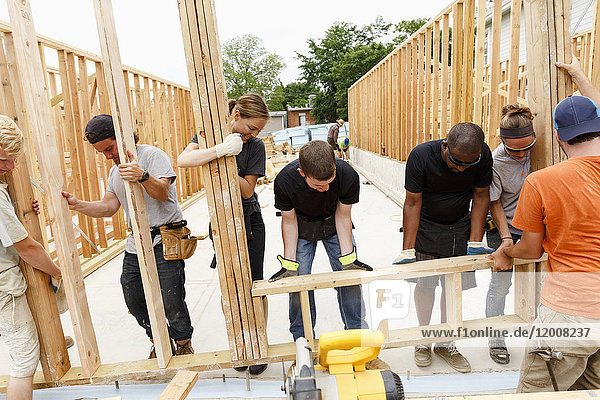 Volunteers lifting framed wall at construction site